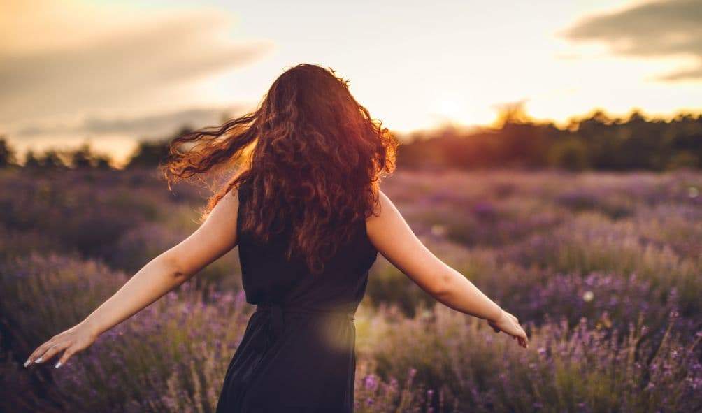 mulher no campo entre flores de braços aberto apreciando a liberdade